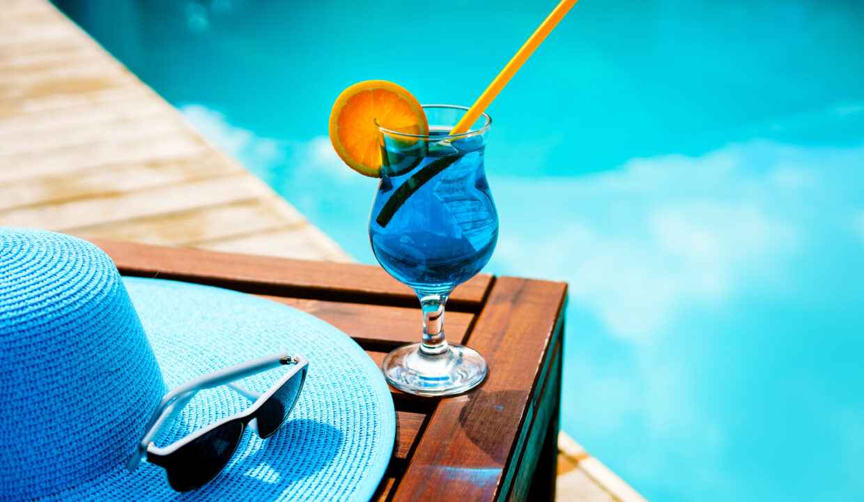 Summer,Hat,,A,Cocktail,And,Sunglasses,Near,The,Luxurious,Pool